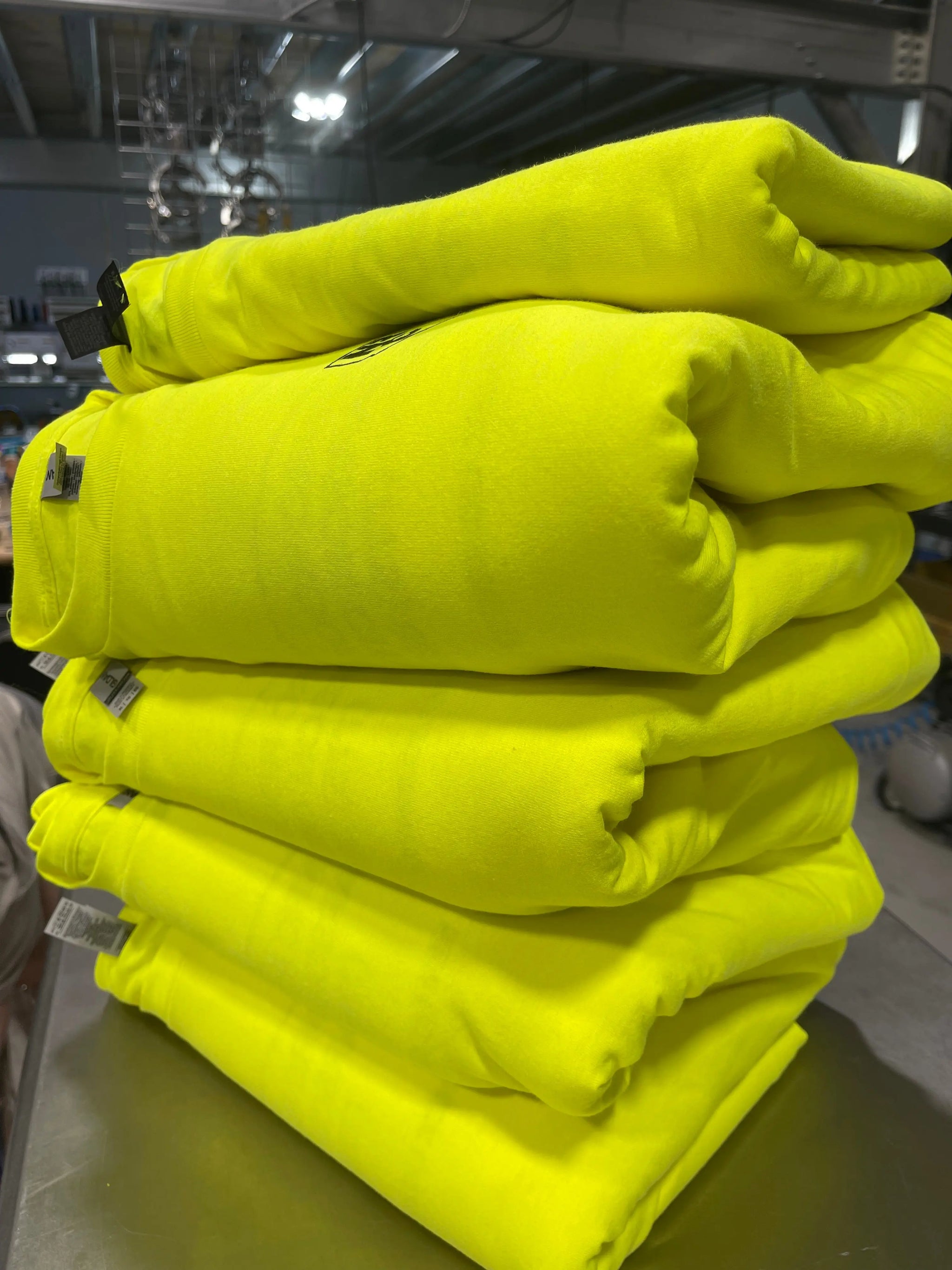 Stack of hi-viz safety tees ready for custom printing at the Game Over Merch production facility.
